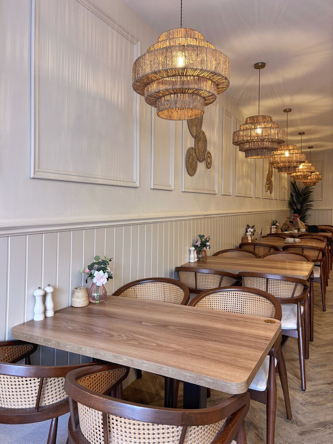 Inside Touché: light wooden tables, cane chairs and woven pendant lights along a cream panelled wall