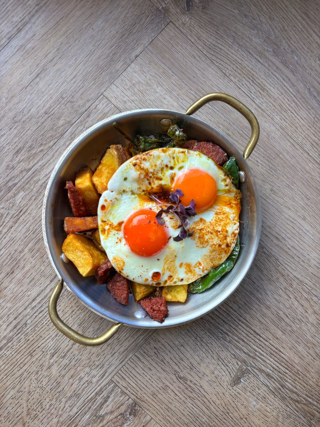 Two fried eggs on crisp potatoes and sucuk in a small pan