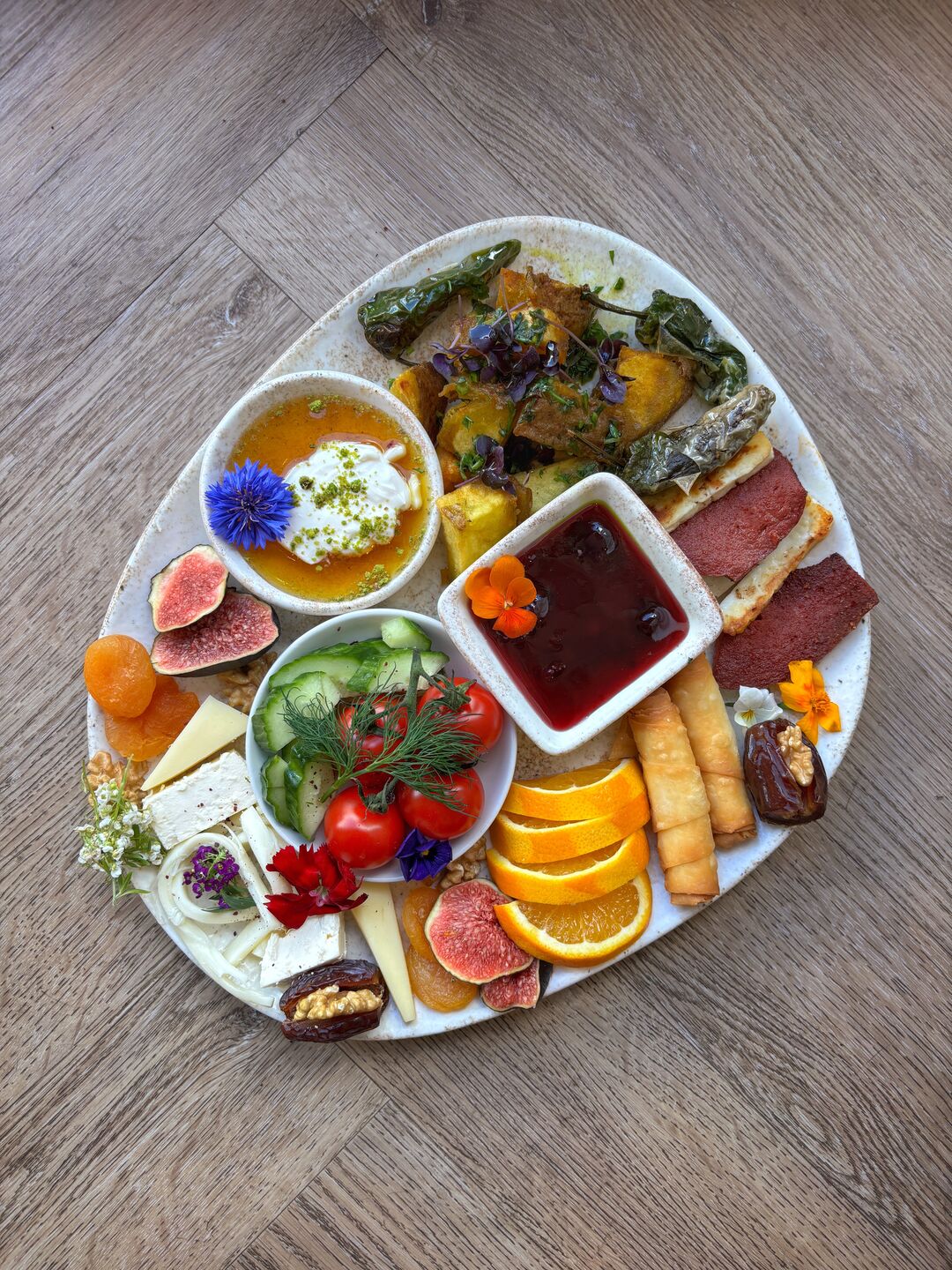 A Turkish breakfast spread on one plate: cheeses, figs, dates, dried apricots, tomatoes and cucumber, jam, honey with cream, fried pastry rolls and orange slices