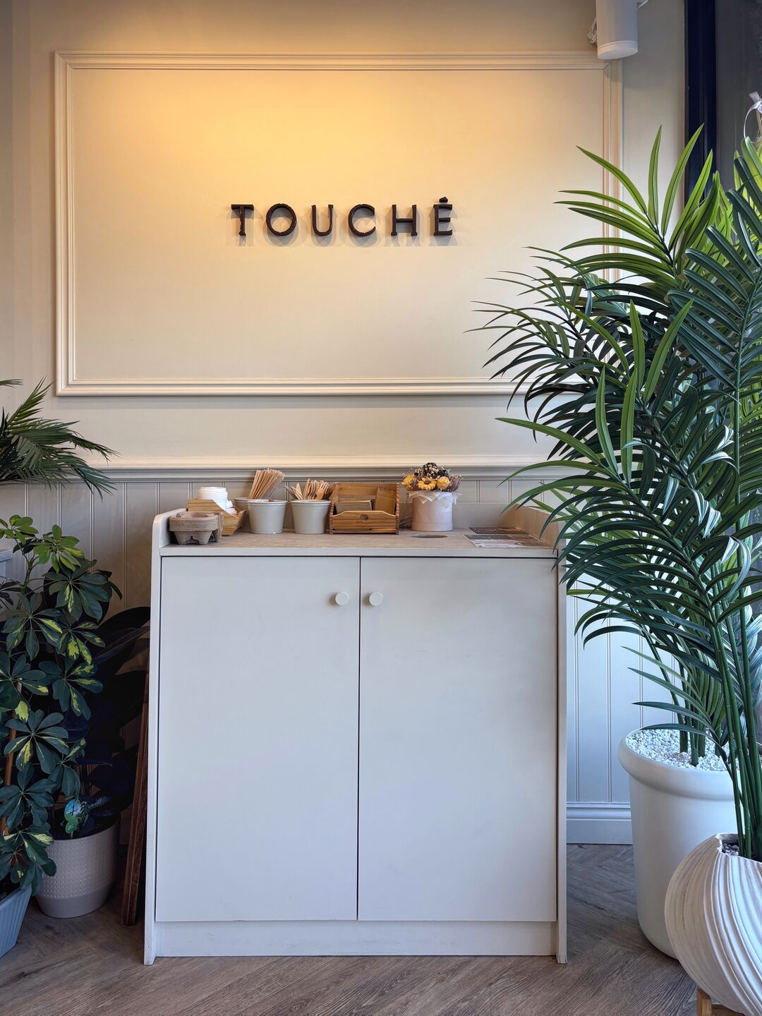 The Touché sign on the café wall, with plants either side